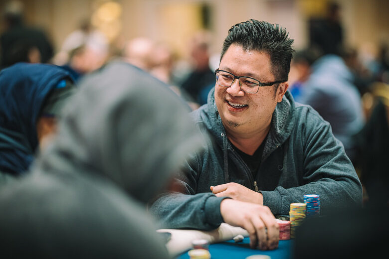 A portrait of Bin Weng, dressed in casual attire, smiling as he sits at a poker table in a tournament.